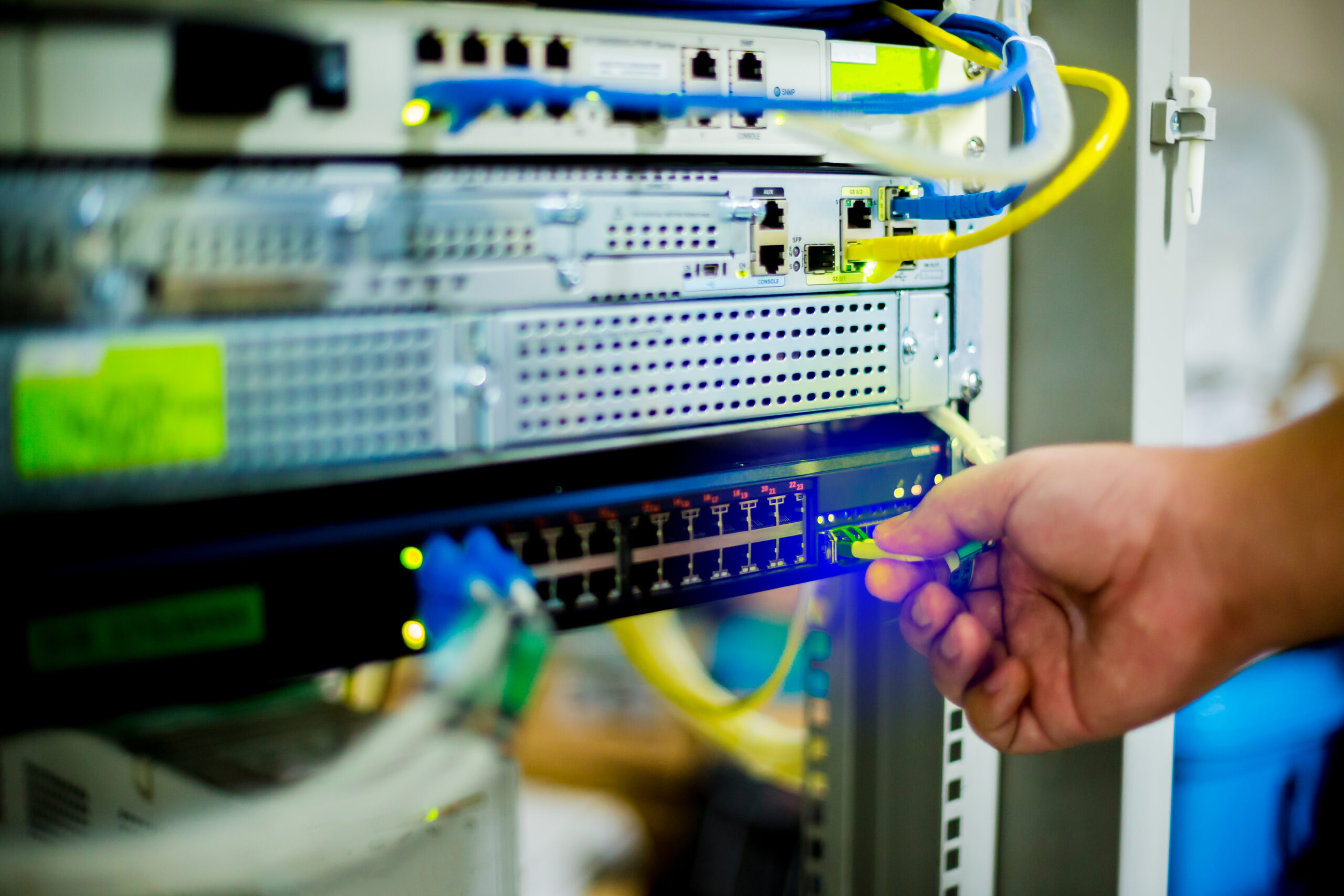 Hand holding fiber optic cord with Ethernet cables and network switching hub. LAN system communication in computer control room. Fiber optic cabling.